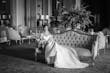 Bride Wearing Simple Off-the-shoulder Wedding Dress Called Josie By Rebecca Ingram Sitting On A Couch