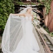Bride stood on railway track holding out her veil wearing wedding dress called Alistaire.