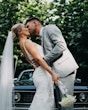 Bride wearing Fontaine by Maggie Sottero kissing her husband in front of a car