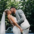 Bride wearing Fontaine by Maggie Sottero kissing her husband in front of a car