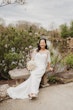 Bride wearing Clover by Rebecca Ingram sitting on a stone bench