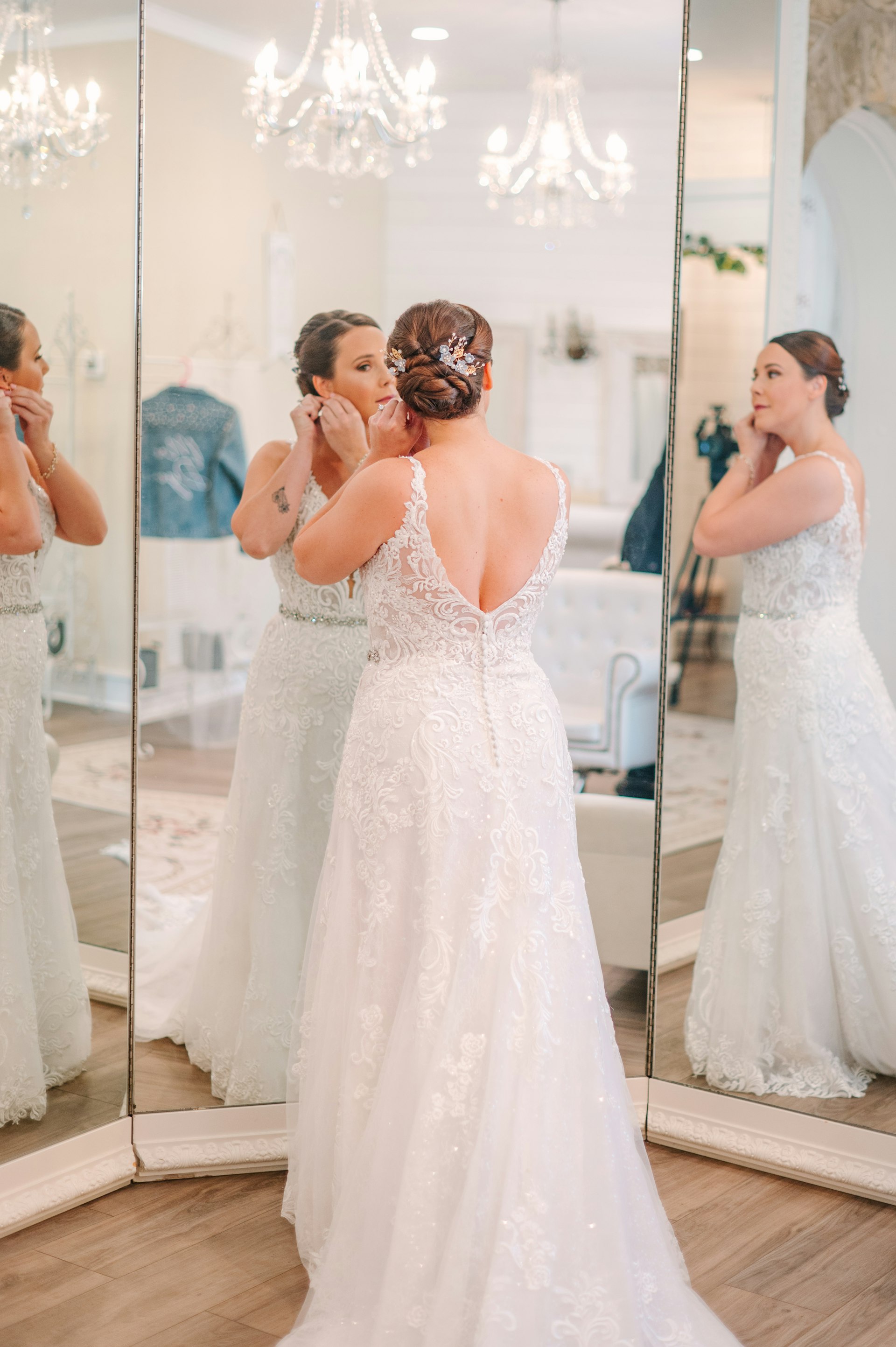 Bride wearing Johanna by Maggie Sottero putting on her earrings in front of a mirror