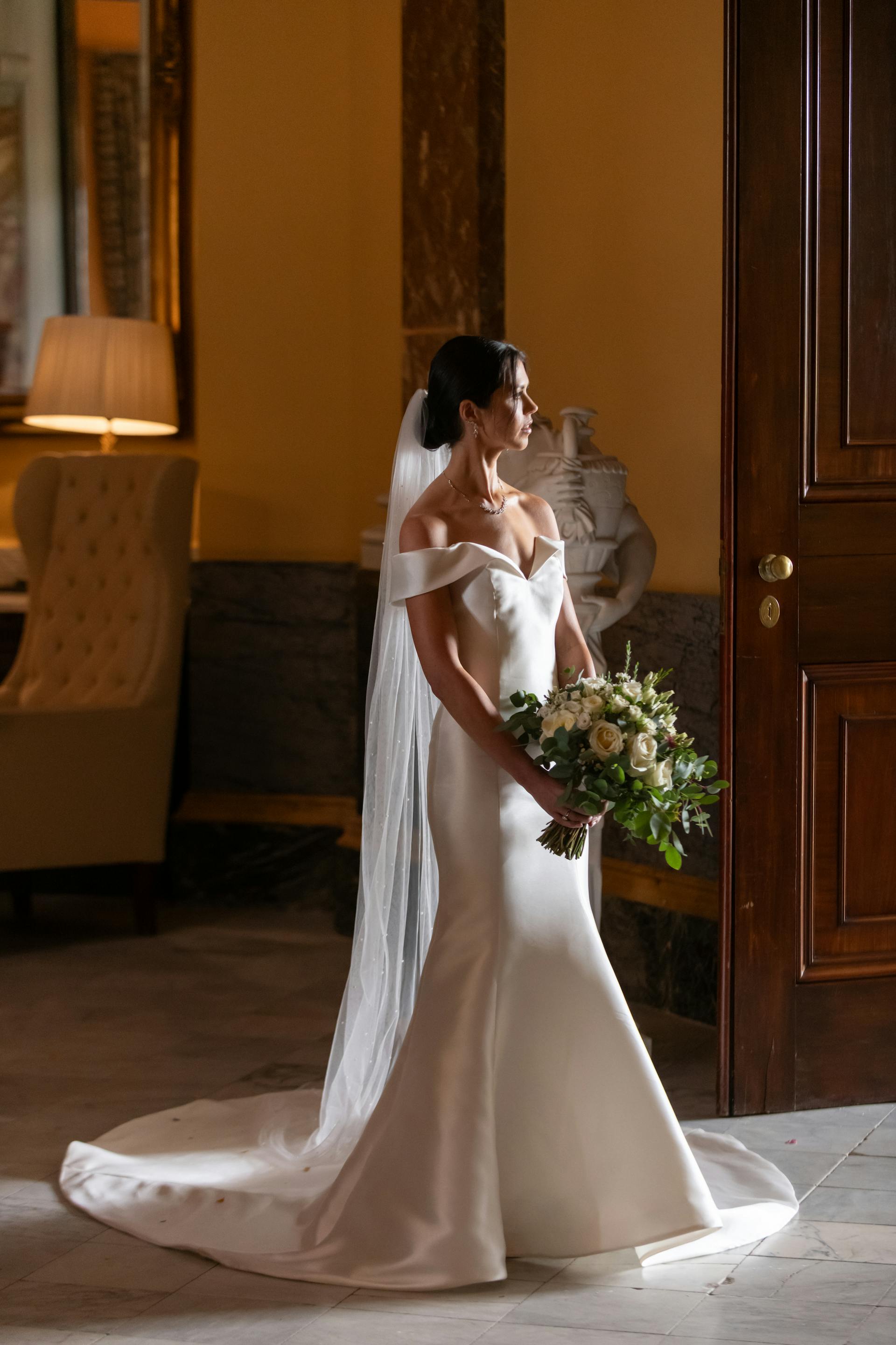 Bride Wearing Simple Off-the-shoulder Wedding Dress Called Josie By Rebecca Ingram Holding Rose Bouquet