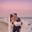 Groom Holding Bride on Sand Beach with Sunset Background Wearing Relaxed Boho Mermaid Wedding Dress called Tuscany by Maggie Sottero.