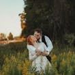 Groom Kissing Bride In Loving Embrace While Standing In Nature. Bride Wearing Illusion Sleeve A-line Wedding Dress Called Raphael By Maggie Sottero