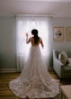 Bride Wearing Lace Long Sleeve Aline Wedding Dress Called Winter By Maggie Sottero Standing Next To A Window