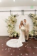 Bride Wearing Lace Fit And Flare Wedding Dress Called Fairchild By Maggie Sottero With Groom Next To A Flower Arch