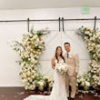 Bride Wearing Lace Fit And Flare Wedding Dress Called Fairchild By Maggie Sottero With Groom Next To A Flower Arch