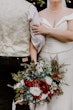 Bride Wearing Simple Fit And Flare Wedding Dress Called Josie By Rebecca Ingram Holding Groom and A Red White And Blue Bouquet