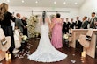 Bride Wearing Lace Fit And Flare Wedding Dress Called Fairchild By Maggie Sottero Walking Down The Aisle With Her Mom In A Floral Pink Dress